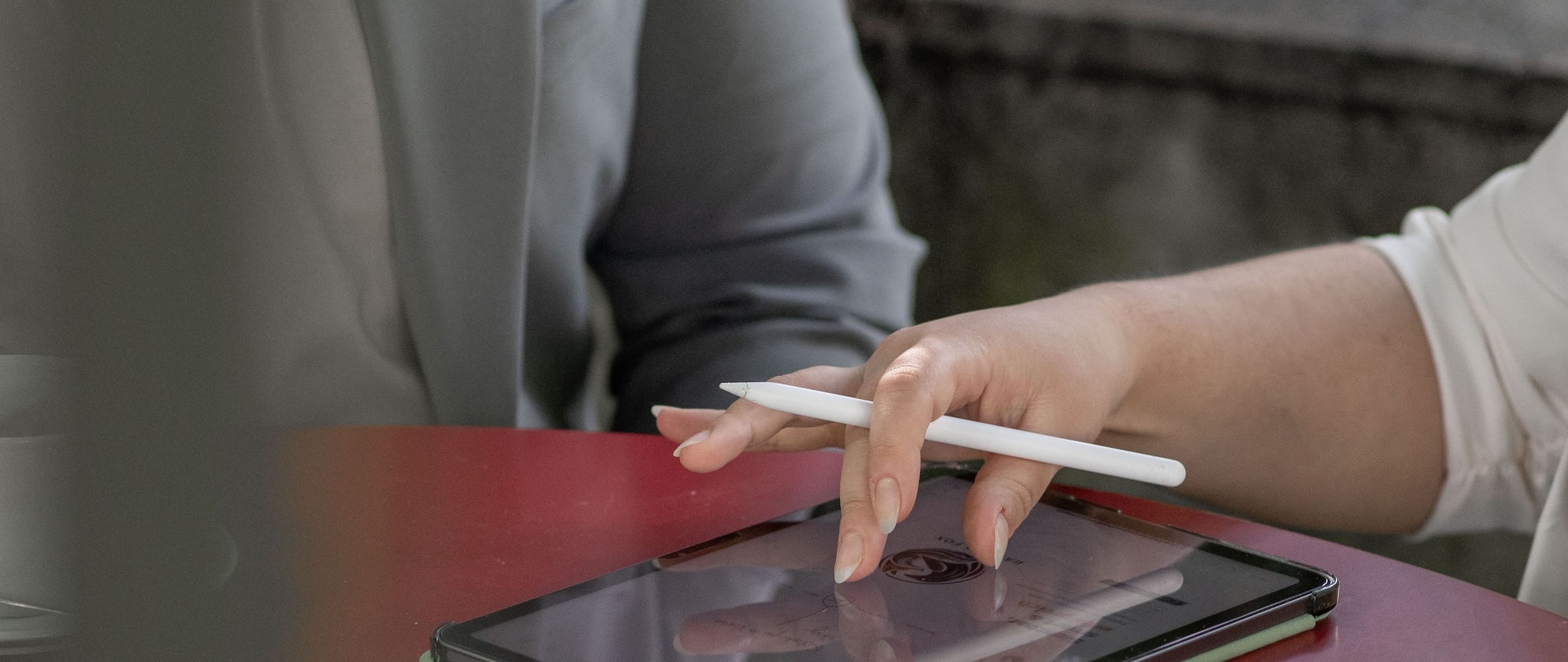 Zwei Personen an einem Tisch, eine Hand führt einen Eingabestift über ein Tablet mit dem Raven & Fox Logo.