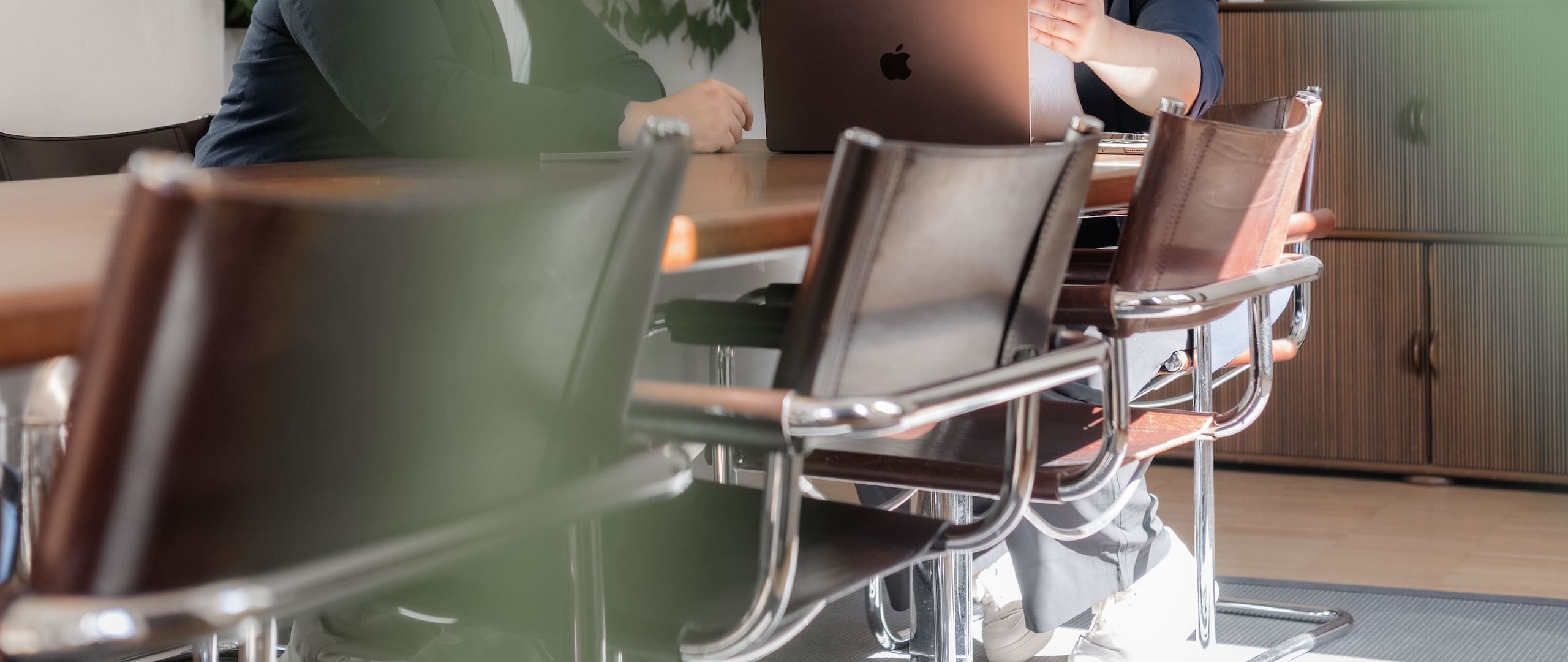 Besprechung am Konferenztisch: Zwei Personen arbeiten gemeinsam an einem Laptop, im Vordergrund leere Freischwinger-Stühle.